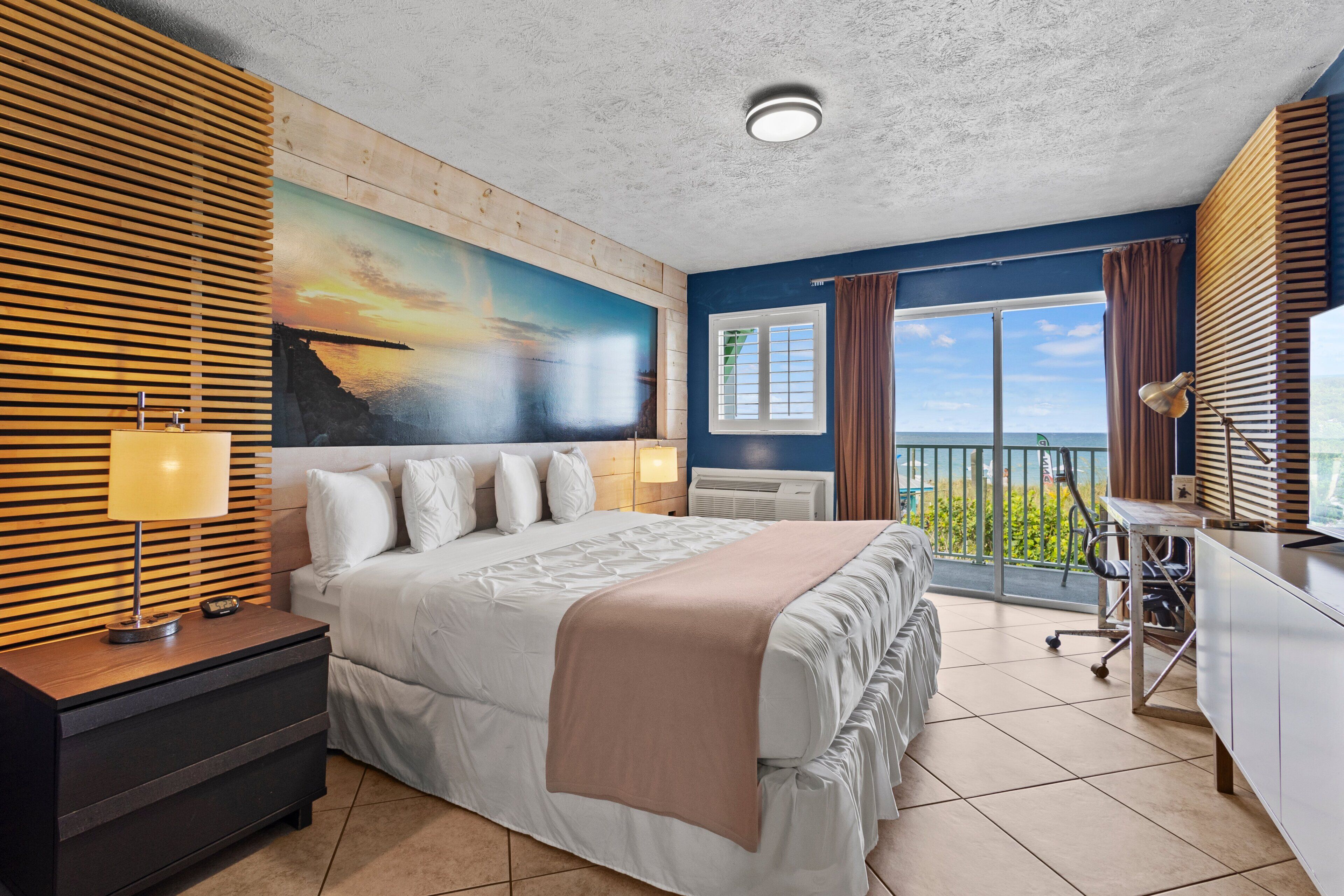 A hotel room with a large bed, a desk, a computer, and a view of the ocean.