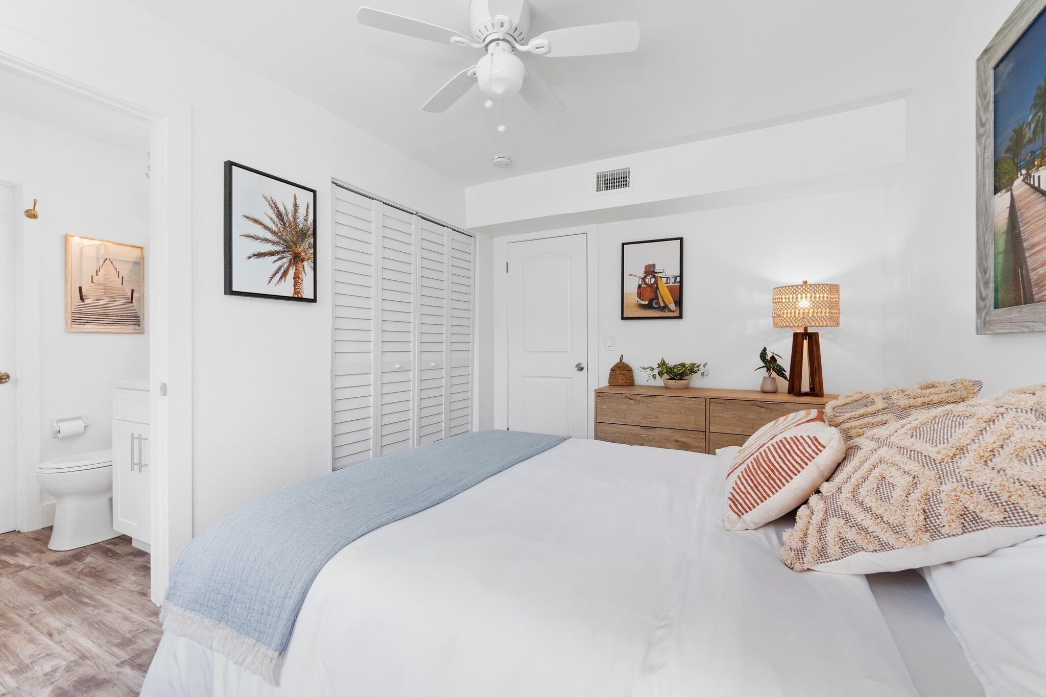 A bedroom with a bed, a ceiling fan, a dresser, and framed pictures on the walls.