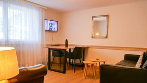 Una sala de estar acogedora con un sofá, una mesita, un televisor montado en la pared y una lámpara.