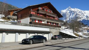 Un hotel de varios pisos con balcones, un estacionamiento y montañas al fondo.
