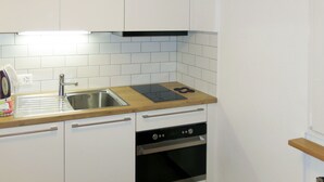 Una cocina compacta con armarios blancos, un lavamanos de acero inoxidable, una encimera negra y un horno integrado.