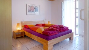 A bedroom with a wooden bed, a nightstand, a wall-mounted lamp, and a window with curtains. - Apartment Wychel by Interhome (Grindelwald)