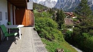 A balcony with a table and chairs, overlooking a village and snow-capped mountains. - Apartment Wychel by Interhome (Grindelwald)