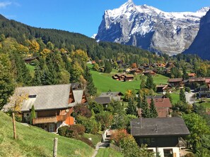 A mountain village with traditional wooden houses, a clear path leading to a chalet, and a snow-capped mountain in the background.