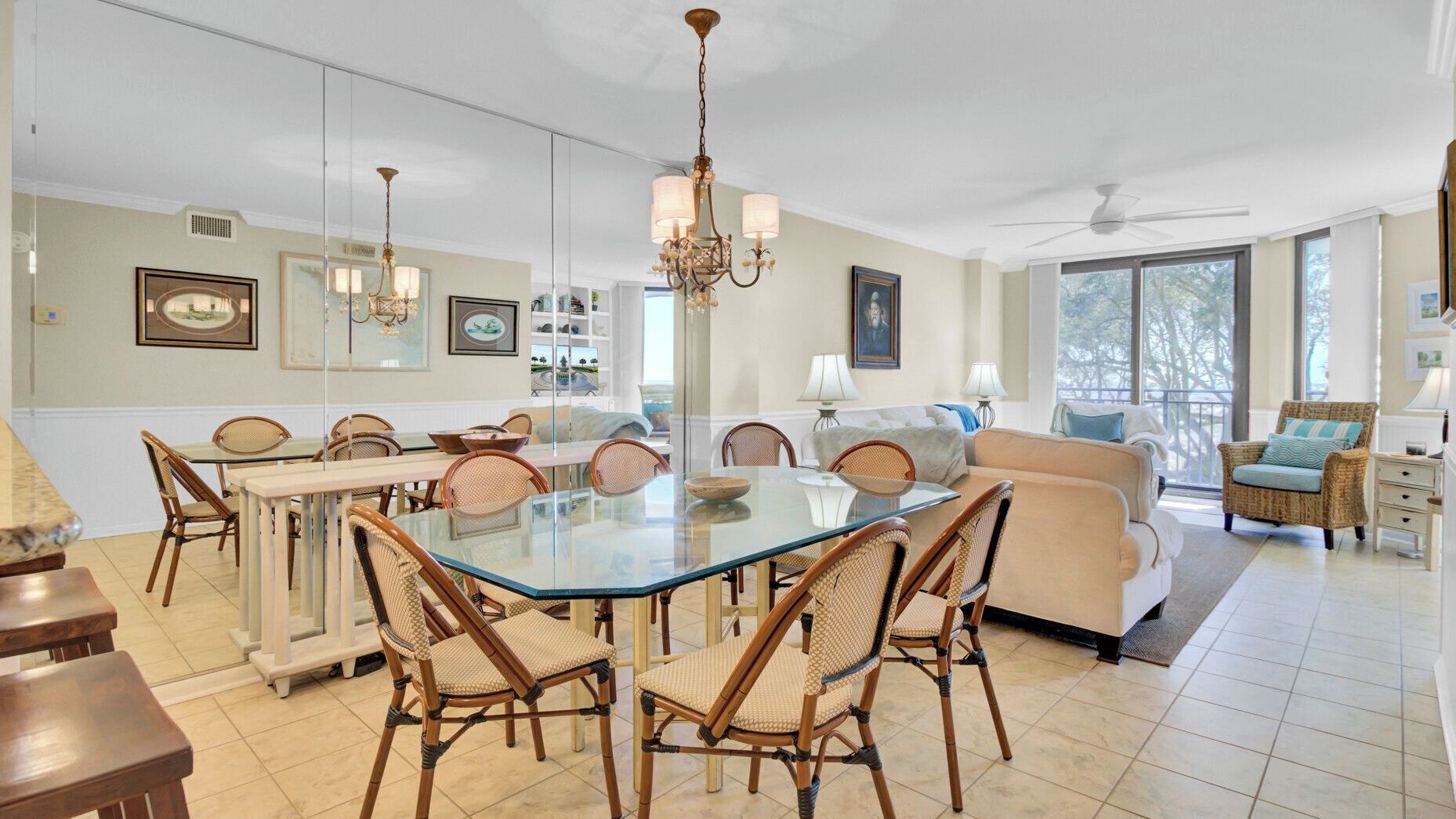 A spacious living area with a glass dining table, wicker chairs, a sofa, and a balcony with a view.