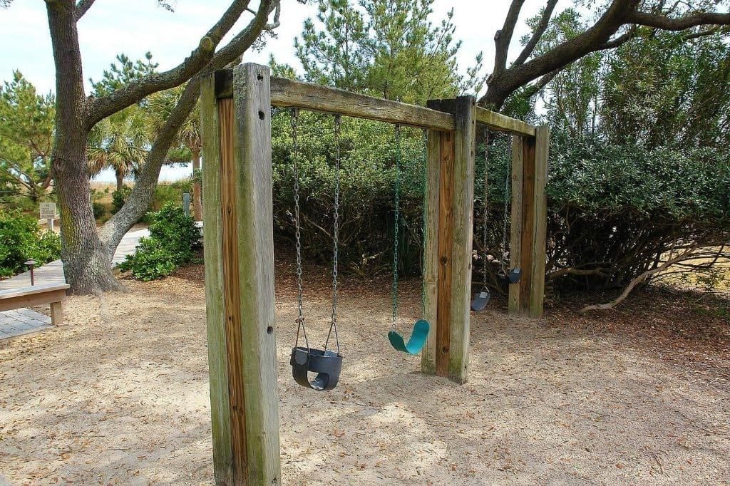 Un ensemble de balançoires en bois installé dans un espace boisé, avec un banc à proximité.