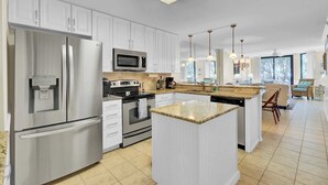 A modern kitchen with white cabinetry, stainless steel appliances, a granite countertop island, and pendant lighting. - 123d Shipwatch by Avantstay Beach Access + Pool (Isle of Palms)