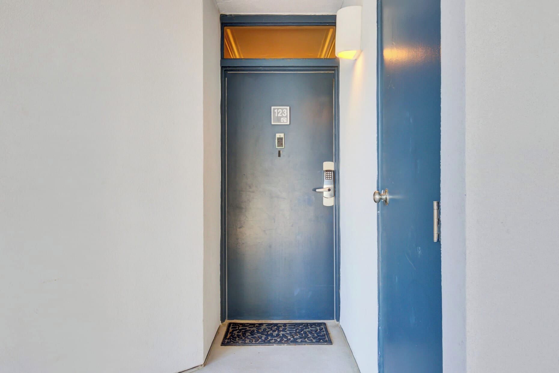Een blauwe deur met een cijferslot, een klein bord met het nummer 123, en een lamp erboven.