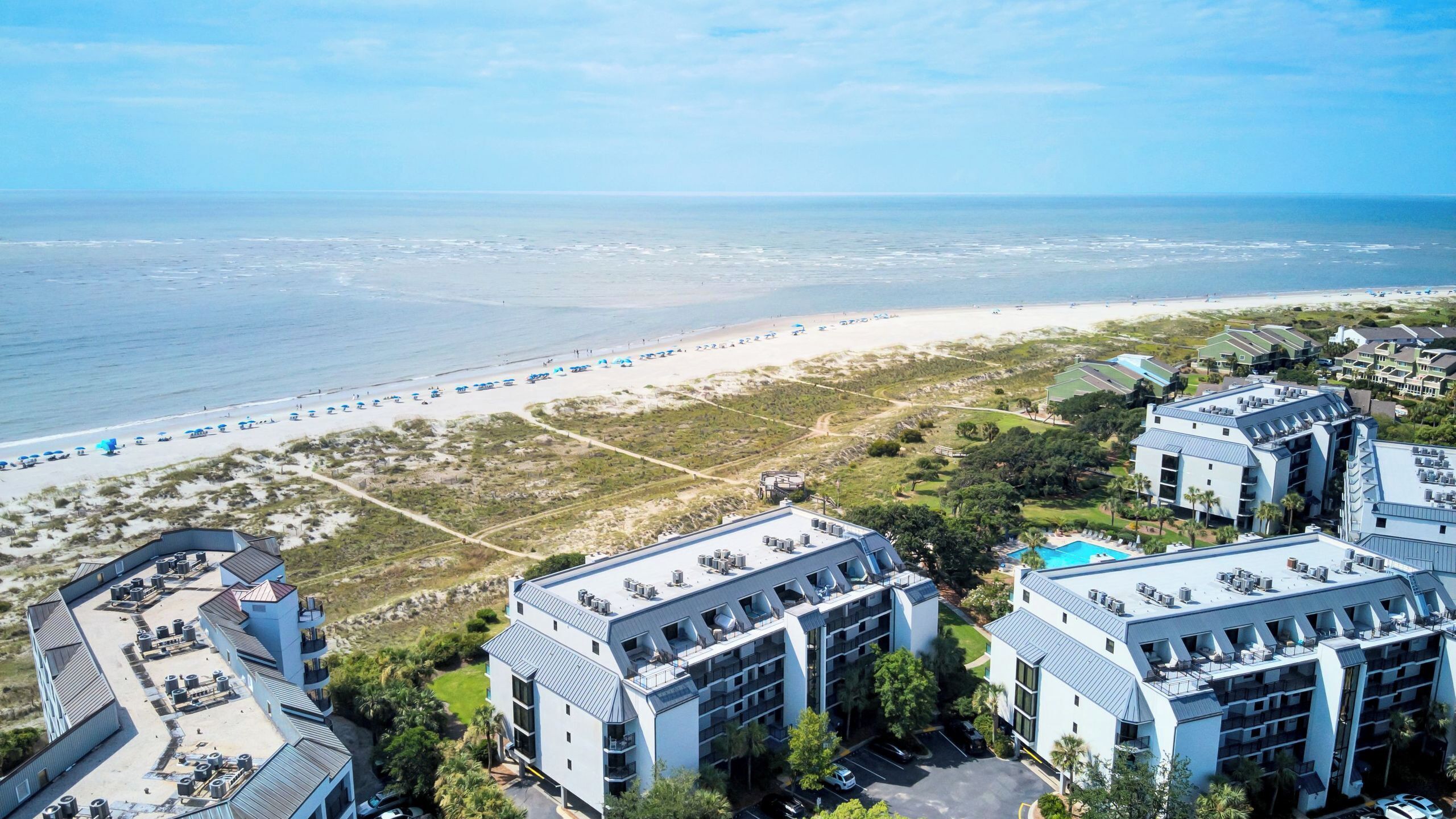 Ein Strandhotel mit mehreren Gebäuden, einem Strand mit Sonnenschirmen und freiem Blick auf den Ozean.