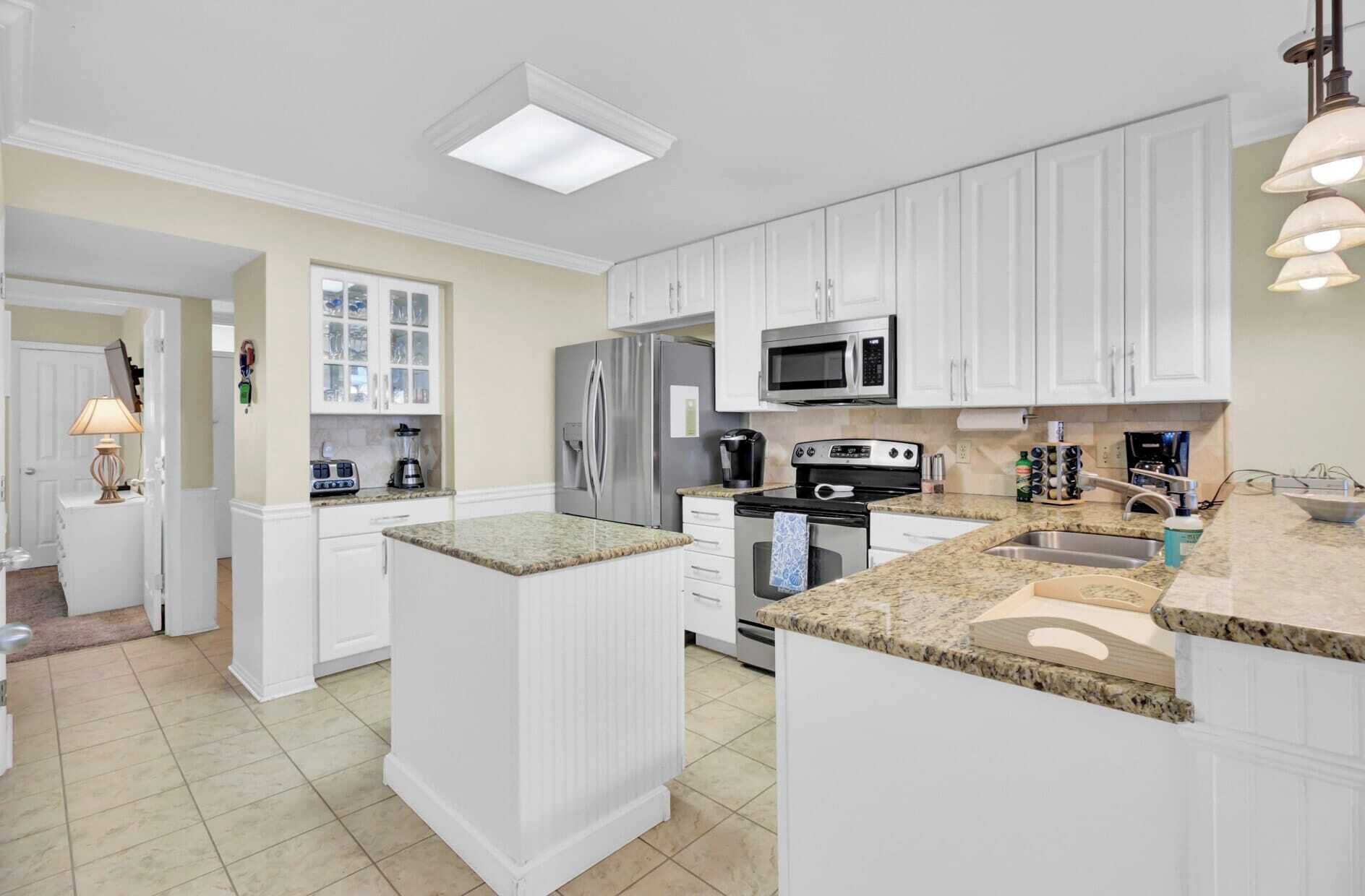 A modern kitchen with white cabinetry, a granite countertop, stainless steel appliances, and a central island.
