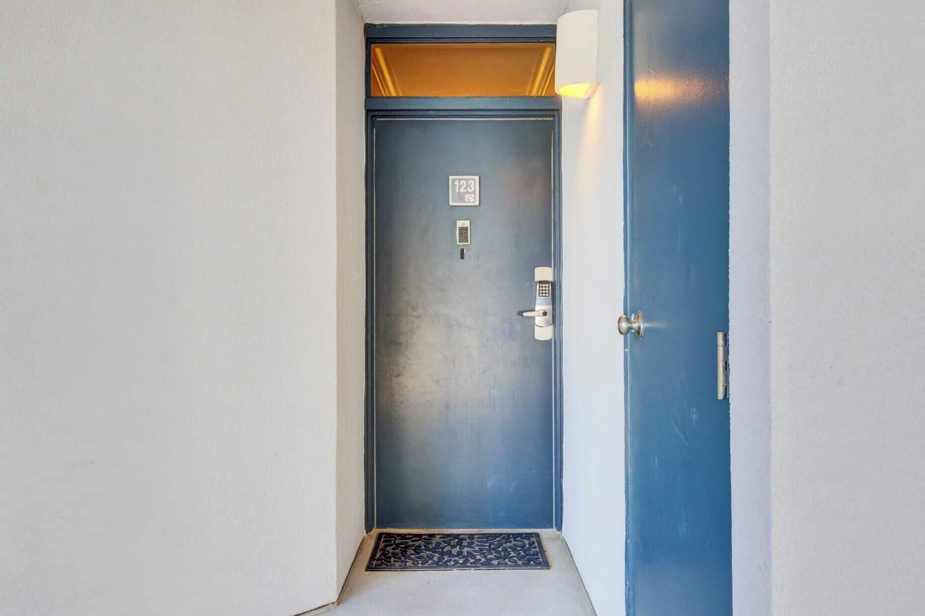 A blue door with a keypad lock, a small sign with the number 123, and a light fixture above it.