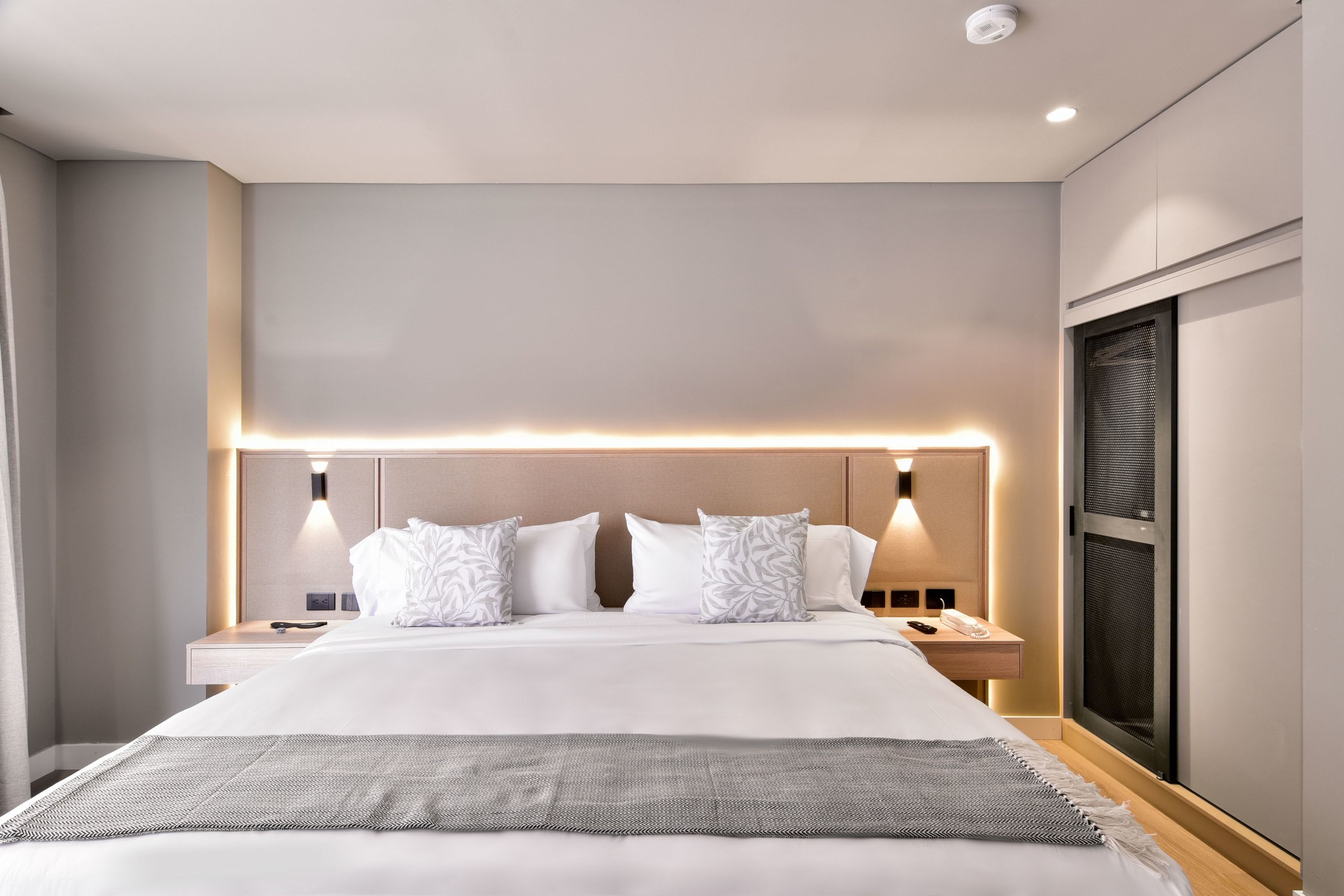 Une chambre d’hôtel moderne dotée d’un grand lit, de tables de chevet et d’une tête de lit avec éclairage intégré.