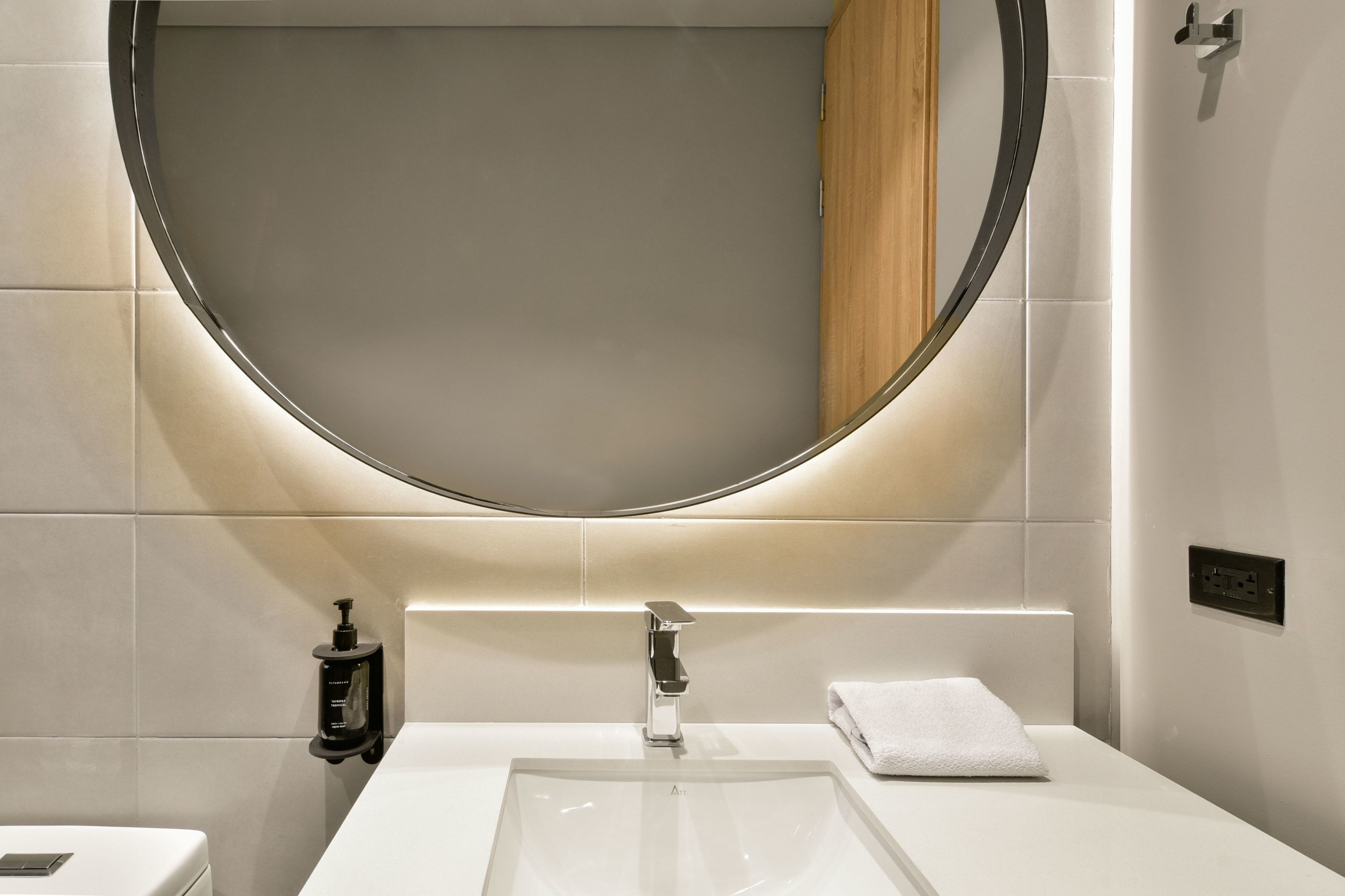 A modern bathroom with a large mirror, a white sink, and a towel.