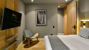 A modern hotel room with a flat-screen TV, a framed abstract artwork, a wooden wardrobe, a bed with a grey blanket, and a wooden chair. - w Illustrious 1BR w/ Great Balcony in Unicentro (Bogotá)