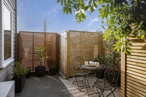A small outdoor patio area with a round metal table and four chairs, surrounded by wooden fences and potted plants.