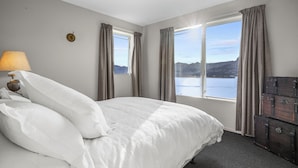 Ein Schlafzimmer mit einem großen Bett, einer Lampe, Blick auf einen See und einem Schminktisch.