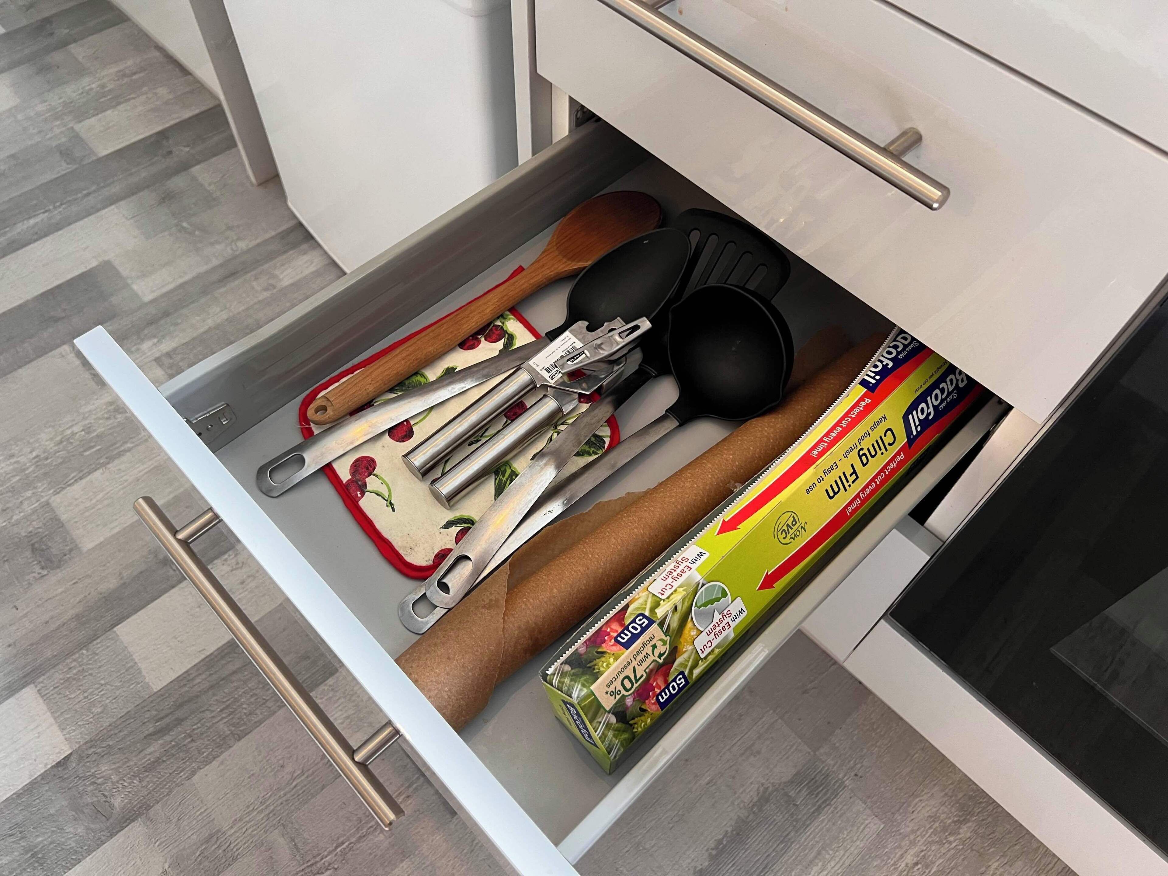 A kitchen drawer containing various utensils, including a wooden spoon, a spatula, and a package of baking paper.