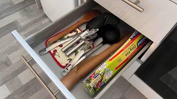 A kitchen drawer containing various utensils, including a wooden spoon, a spatula, and a package of baking paper.