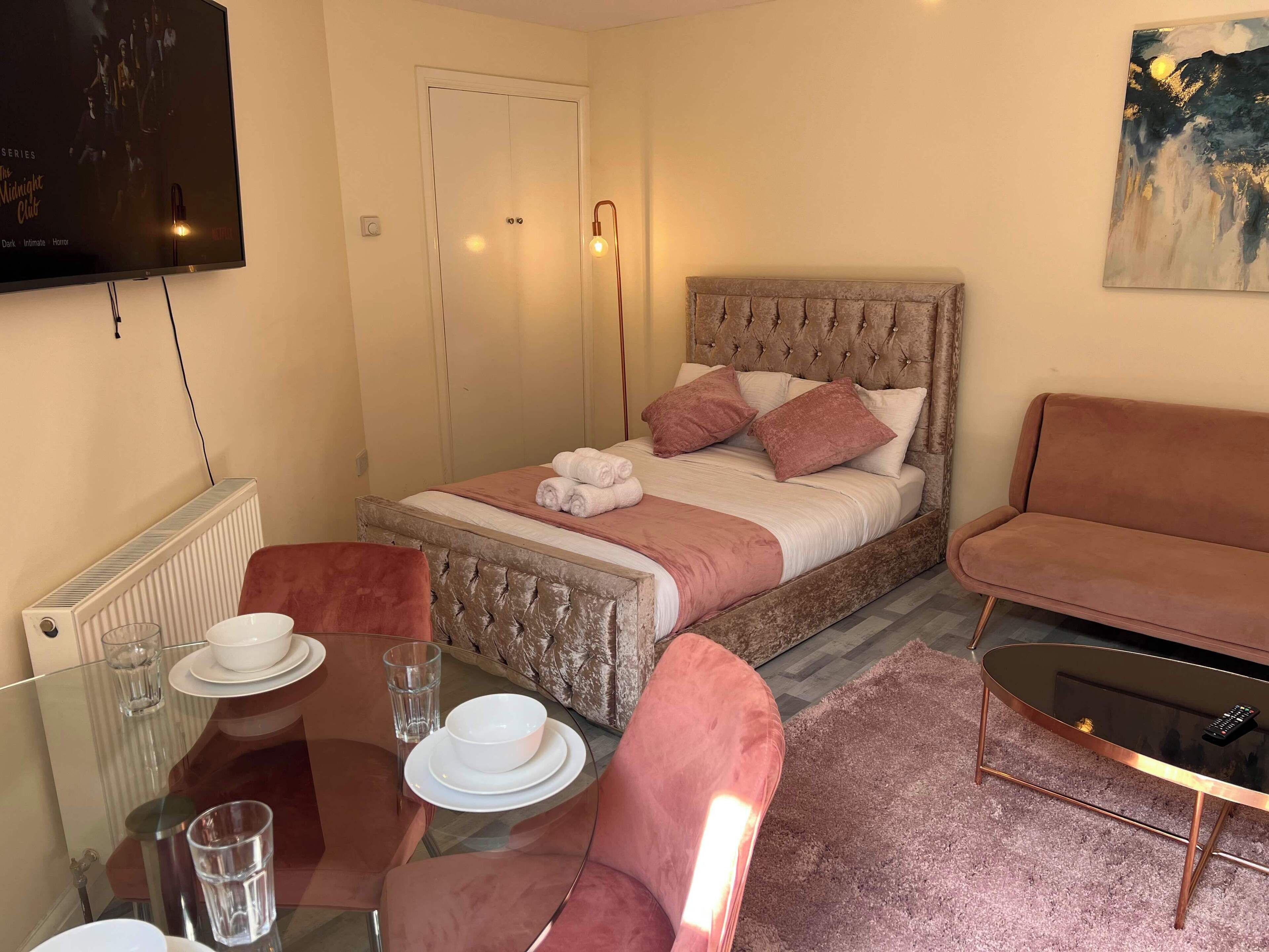 Un dormitorio con cama, sofá, mesa de vidrio con platos y vasos, radiador y televisor en la pared.