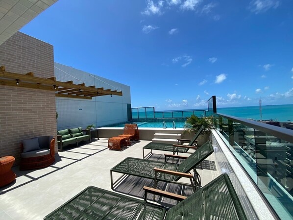 A rooftop terrace with outdoor seating, a pool, and a view of the ocean. - Smart Stay Apto 405 Mandi Hospitalidade (Maceió)