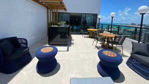 Una terraza en la azotea con mobiliario exterior, una zona de bar y vistas al océano.