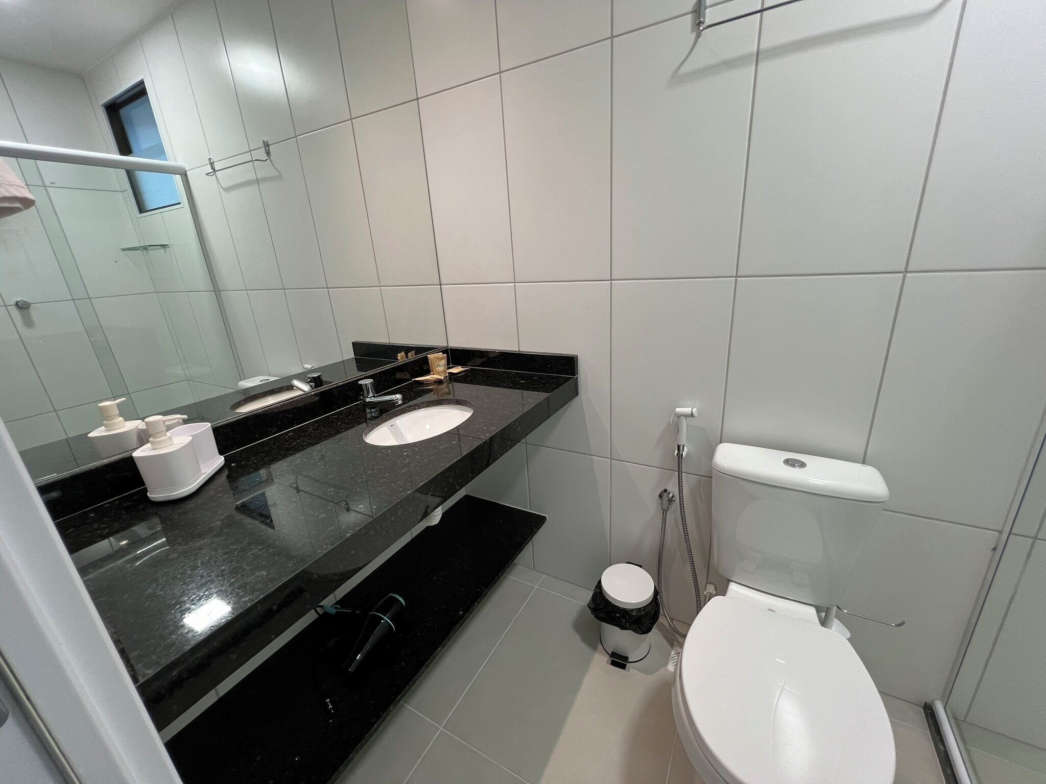 A modern bathroom with a black countertop, two sinks, a toilet, and a shower.