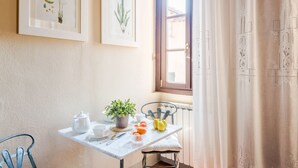 Un coin repas avec une table dressée pour deux personnes, une plante en pot et une fenêtre avec des rideaux.