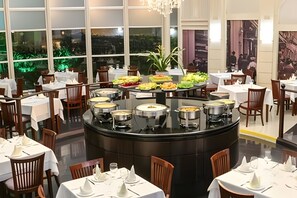 Un restaurant avec des tables rondes, un buffet proposant divers plats et une vue sur la verdure environnante.