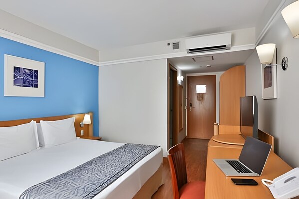 Une chambre d’hôtel équipée d’un lit, d’un bureau avec un ordinateur portable, d’un téléphone et d’une télévision.