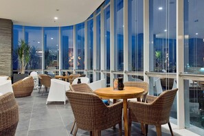 Un espace de détente intérieur moderne, doté de meubles en osier et de grandes fenêtres offrant une vue sur la ville.