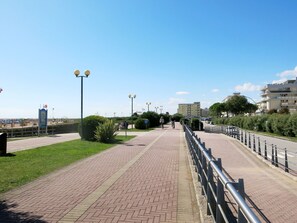 Un chemin pavé bordé d’une rambarde en métal, de l’herbe verte et un ciel bleu dégagé.