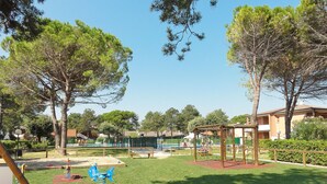 A park with playground equipment, a small pool, and surrounding trees. - Villaggio Azzurro by Interhome (Bibione)