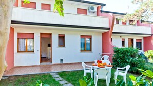 A two-story building with a red and white facade, a small garden with a table and chairs, and a paved walkway. - Villaggio Azzurro by Interhome (Bibione)