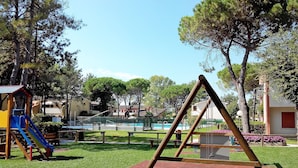 A playground with swings and a slide, surrounded by grass and trees. - Villaggio Azzurro by Interhome (Bibione)