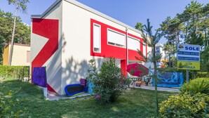 A modern building with a red and white facade, a small garden area with a blue play structure, and a sign advertising a tourist agency.