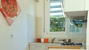 A modern kitchen with white cabinets, a window with a view of greenery, and a red and white decorative piece on the wall.