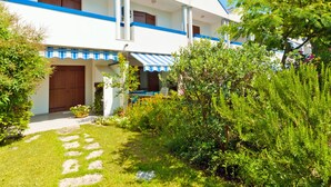 A two-story building with a blue and white exterior, a covered porch, and a well-maintained garden with a stone pathway. - Villaggio Maja by Interhome (Bibione)