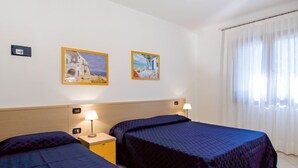 A hotel room with two beds, a nightstand with a lamp, and two framed pictures on the wall. - Villa Angela by Interhome (Bibione)