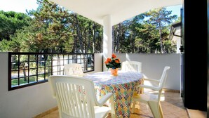 A balcony with a table and chairs, a vase of flowers, and a view of trees. - Villa Angela by Interhome (Bibione)