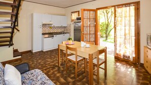 Eine kompakte Küche mit weißen Schränken und einem eingebauten Backofen, ein Esstisch mit Stühlen sowie eine Treppe, die in ein Obergeschoss führt.