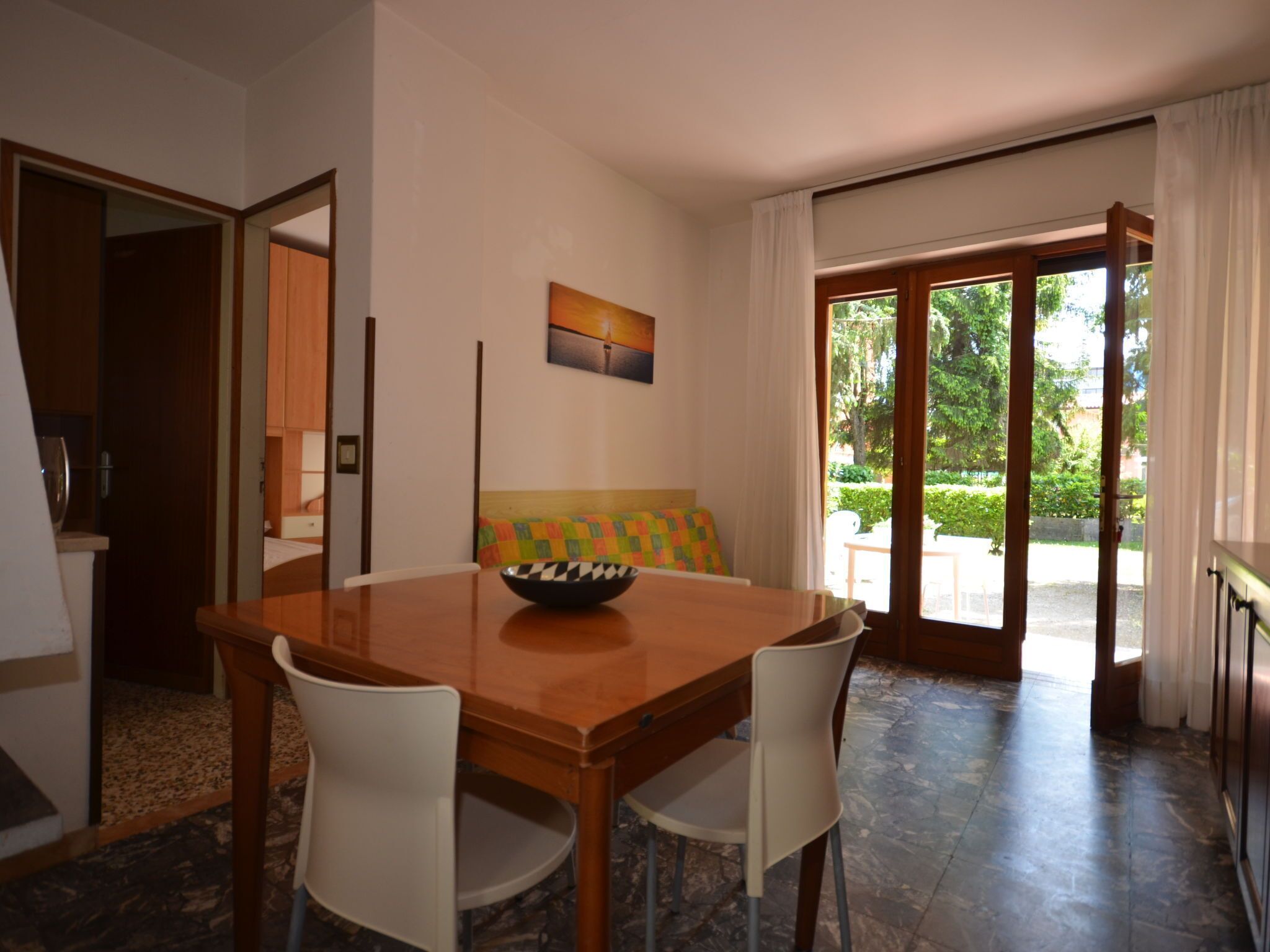 Un coin repas avec une table en bois et deux chaises blanches, un coussin coloré et un bol posé sur la table.