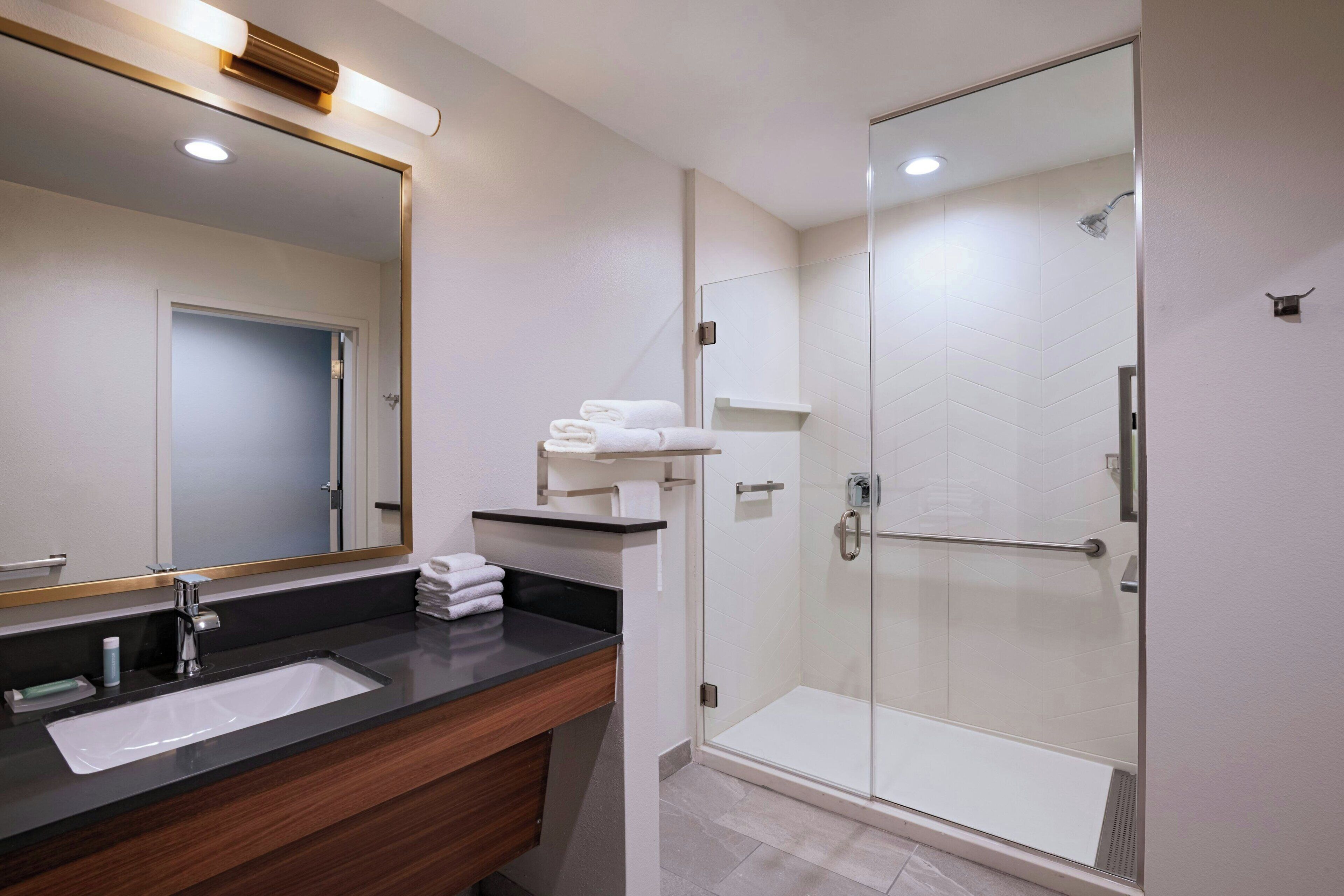 A modern bathroom with a large mirror, a sink, and a glass-enclosed shower.