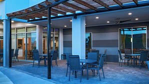 Un patio al aire libre con mesas y sillas, una pérgola y un ventilador de techo.