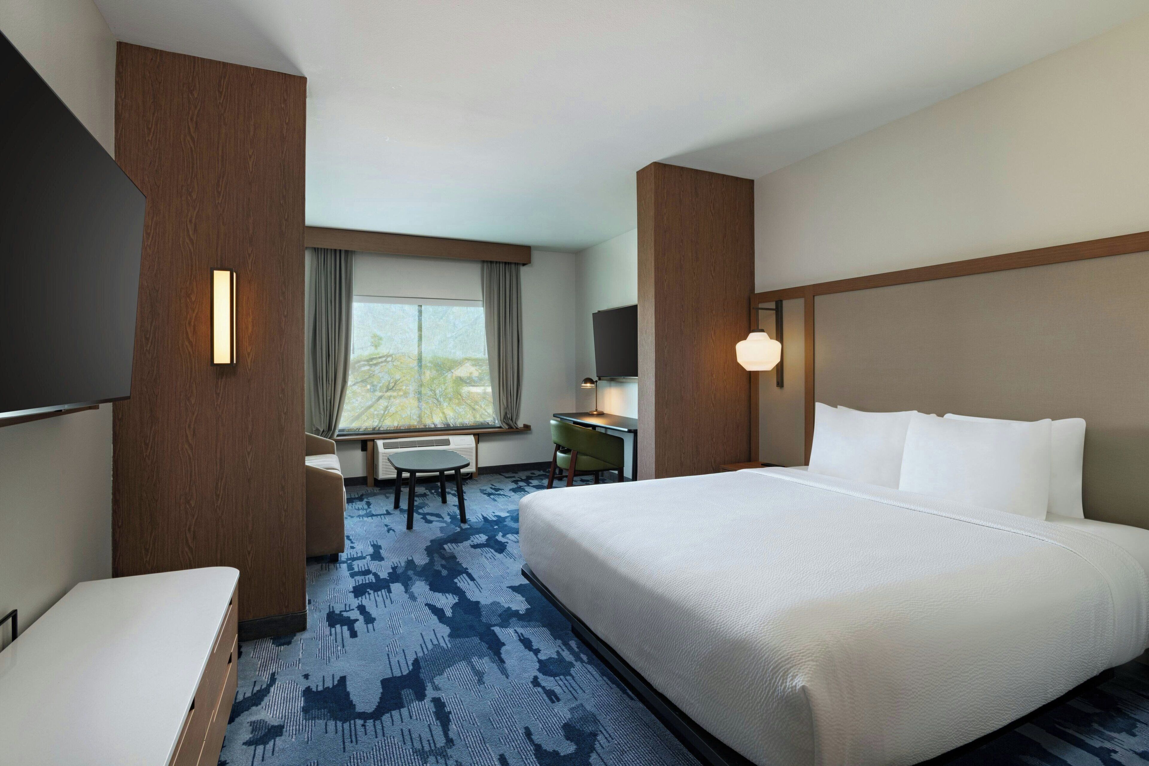 Habitación de hotel con una cama grande, un escritorio, una silla, un televisor y una ventana con cortinas.