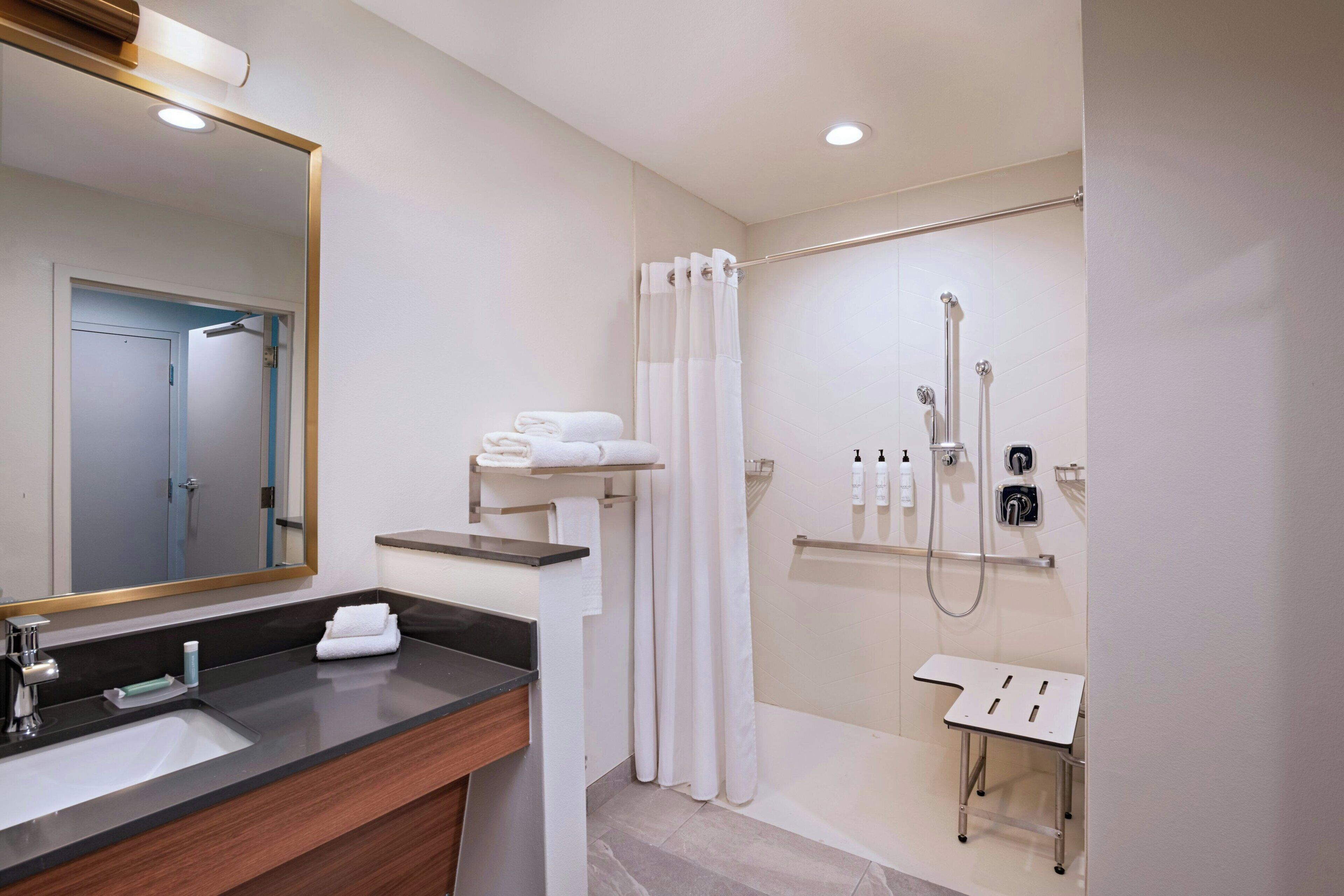 A modern bathroom with a sink, mirror, shower, and towel rack.