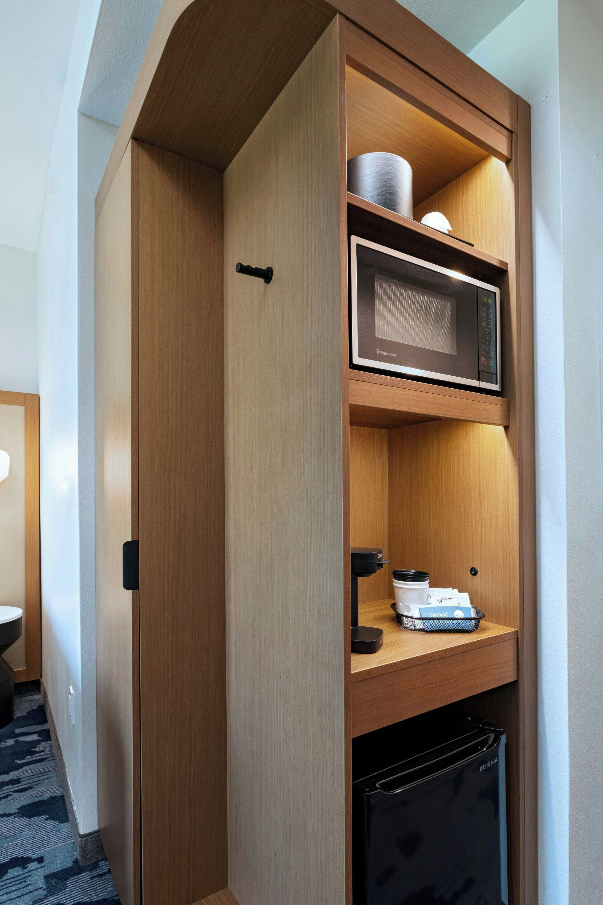 Una kitchenette compacta con microondas, un refrigerador pequeño y una cafetera en un estante.