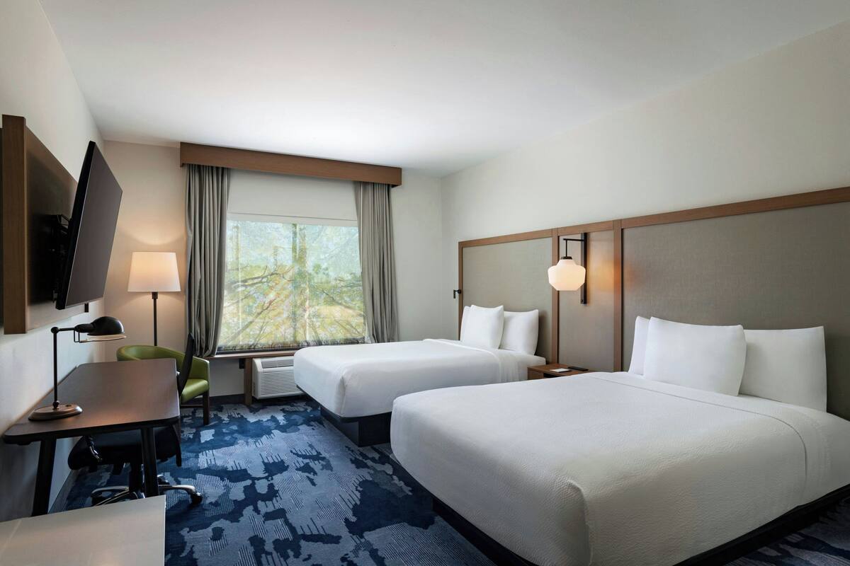 A hotel room with two beds, a desk, a chair, a TV, and a window with curtains.