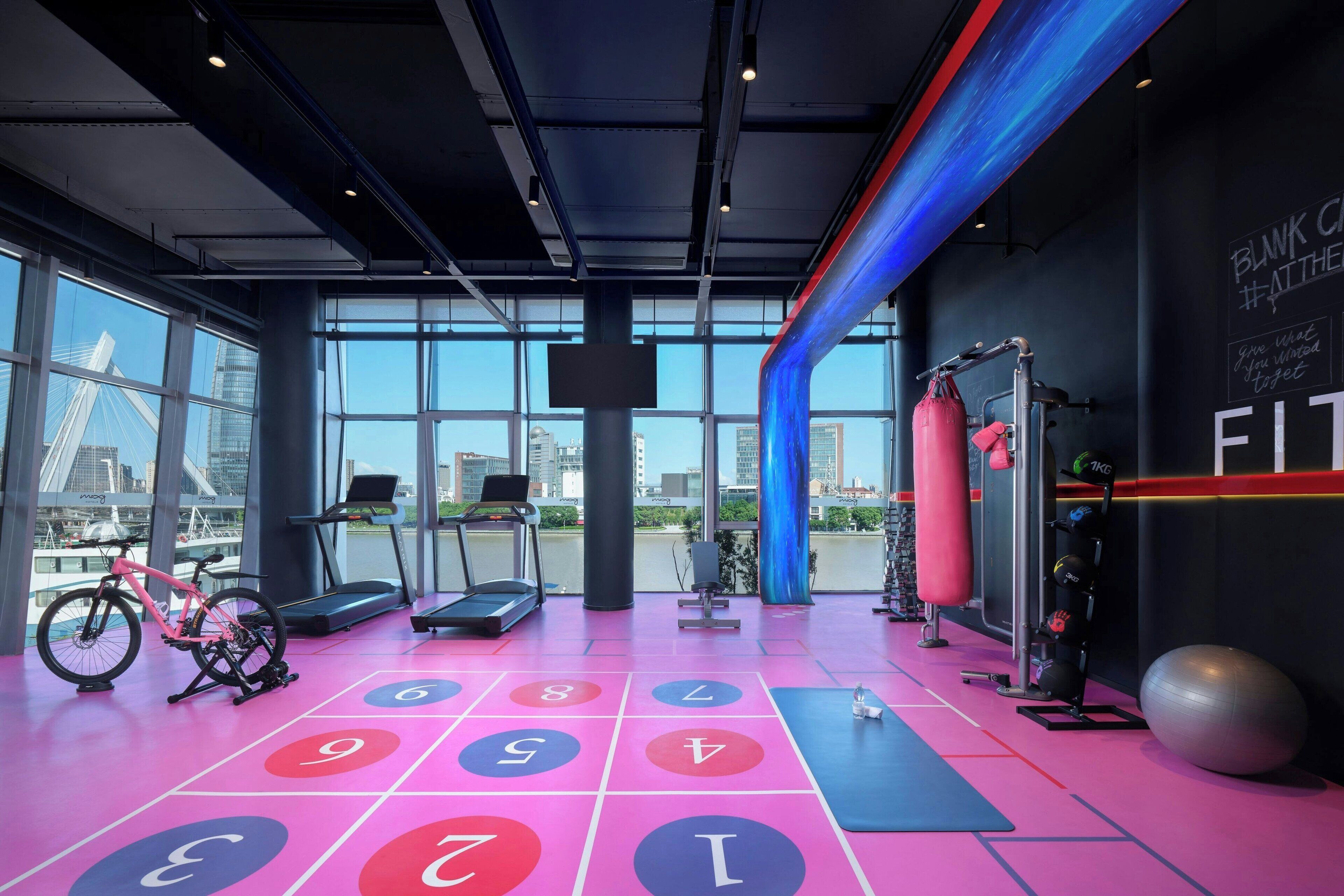 Ett modernt gym med träningsutrustning, ett stort fönster och utsikt över staden.
