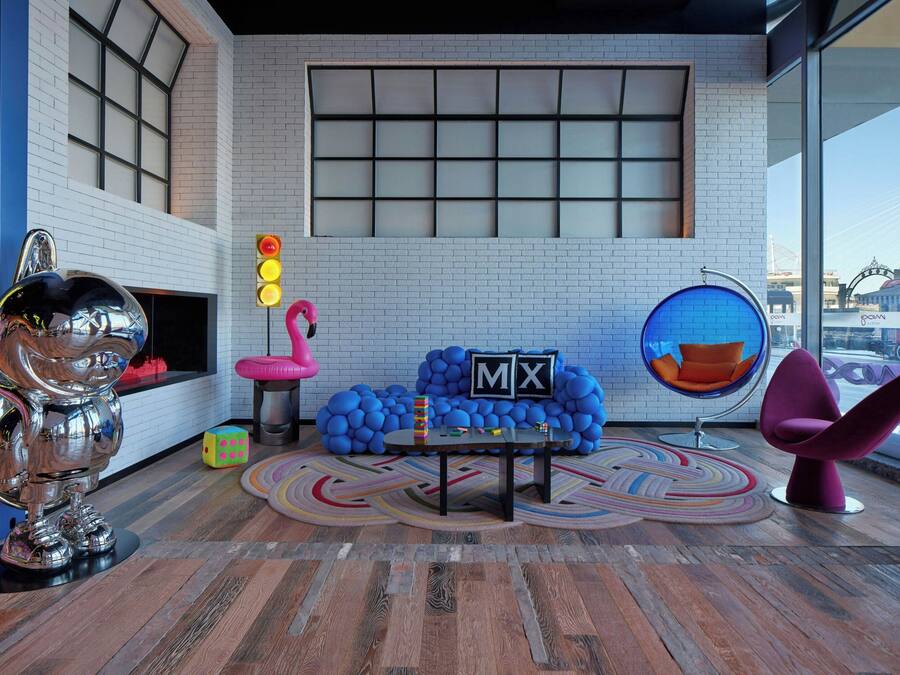 A modern room with a white brick wall, a large window, a round table, and a blue chair.