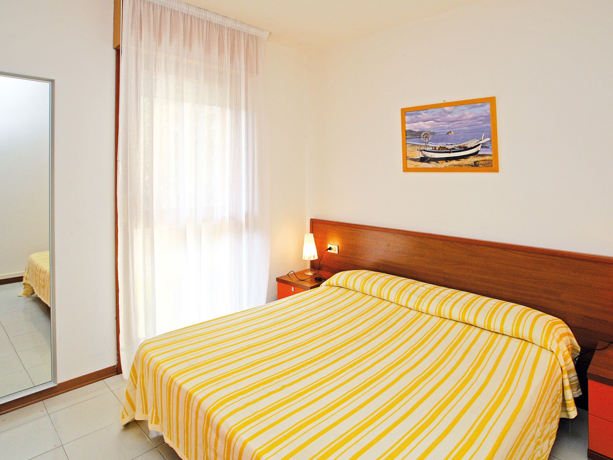 A hotel room with a bed, a nightstand, a lamp, a painting, and a window with curtains.